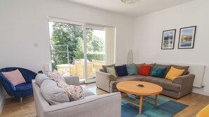 A modern living room with a grey sofa, a blue armchair, a round wooden coffee table, and a brown sofa with colorful cushions. - Hillcrest (Wrexham)