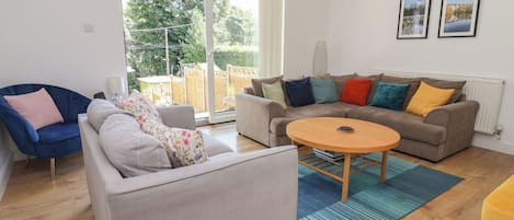A modern living room with a grey sofa, a blue armchair, a round wooden coffee table, and a brown sofa with colorful cushions.