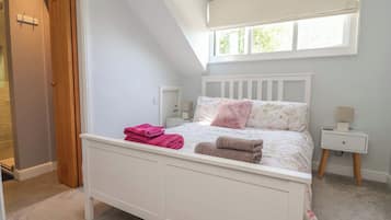 A bedroom with a white bed, a nightstand, a window with blinds, and a door.