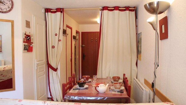 Un comedor con una mesa preparada para cuatro, un reloj en la pared y cortinas con ribete rojo.