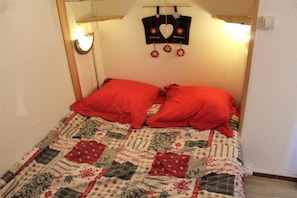 A bed with a quilted bedspread featuring floral and geometric patterns, two red pillows, and a hanging decoration with a heart and snowflakes. - Resort center, 1st floor, balcony, tv, 30m², Vars (Vars)