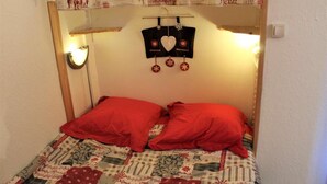 Una cama con almohadas rojas y colcha, un reloj en la pared, y un cartel con un jinete a caballo.