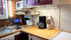 Una cocina compacta con armarios de madera, microondas, cafetera, tostadora y pileta.