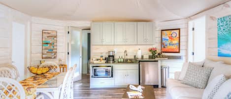A spacious living area with a dining table, white chairs, a sofa, and a kitchen in the background.