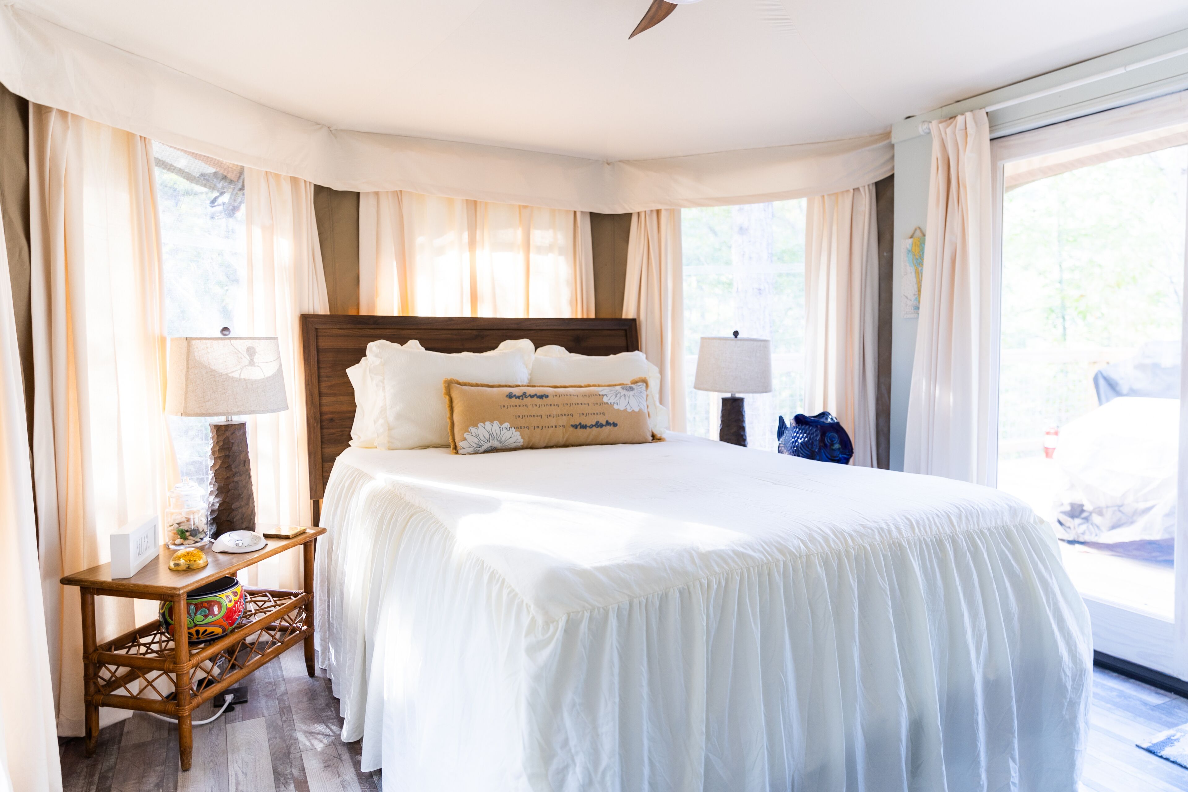 Una habitación de hotel con una cama grande, dos lámparas de noche, una mesita de noche de madera y una ventana con cortinas.