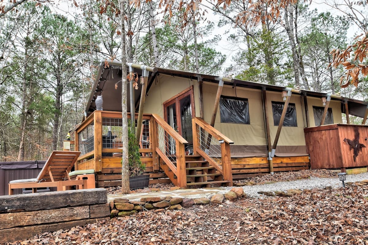 A rustic cabin with a wooden deck, a covered porch, and a hot tub.