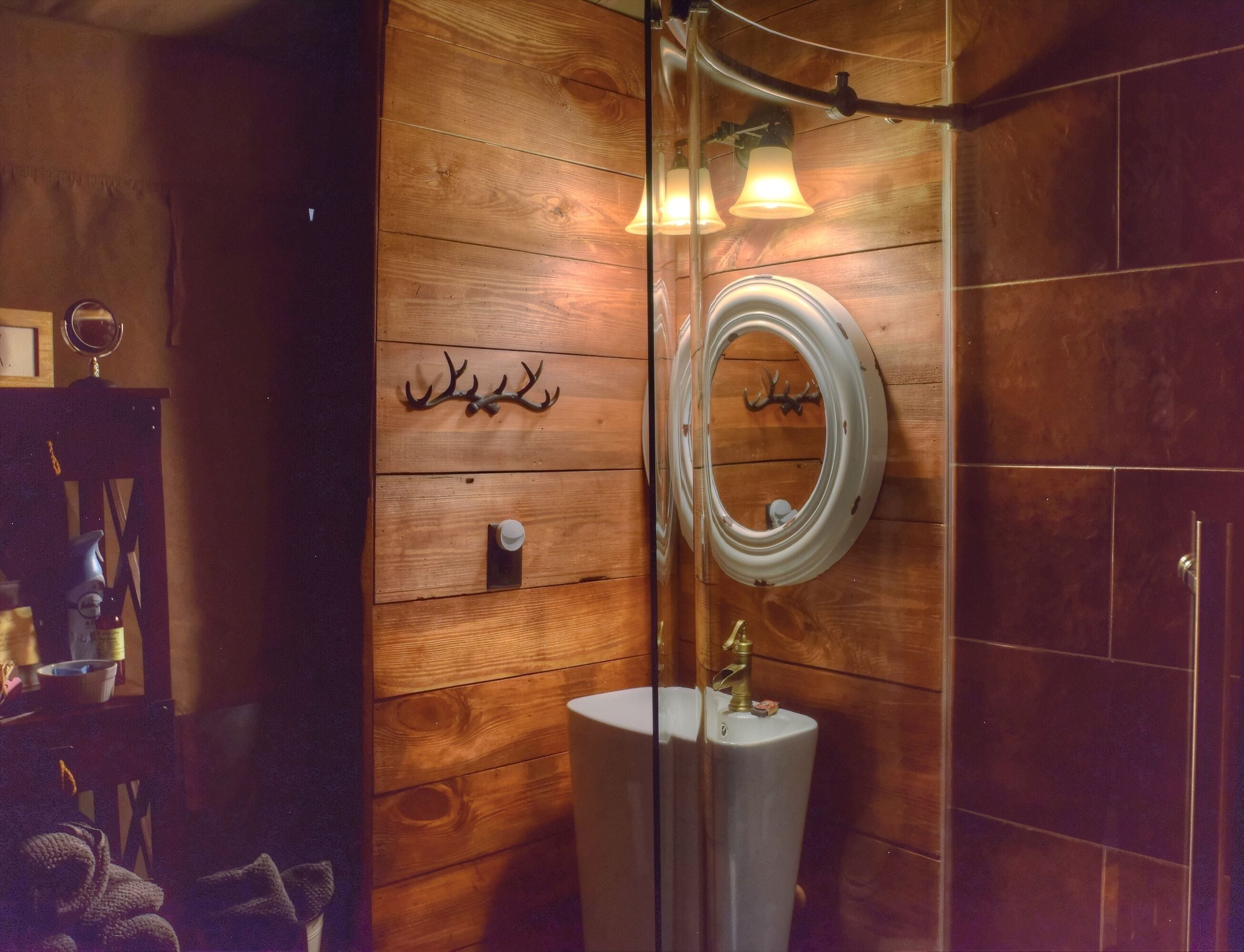 Une salle de bain avec un lambris en bois, un miroir, un lavabo avec un robinet et un luminaire fixé au mur.