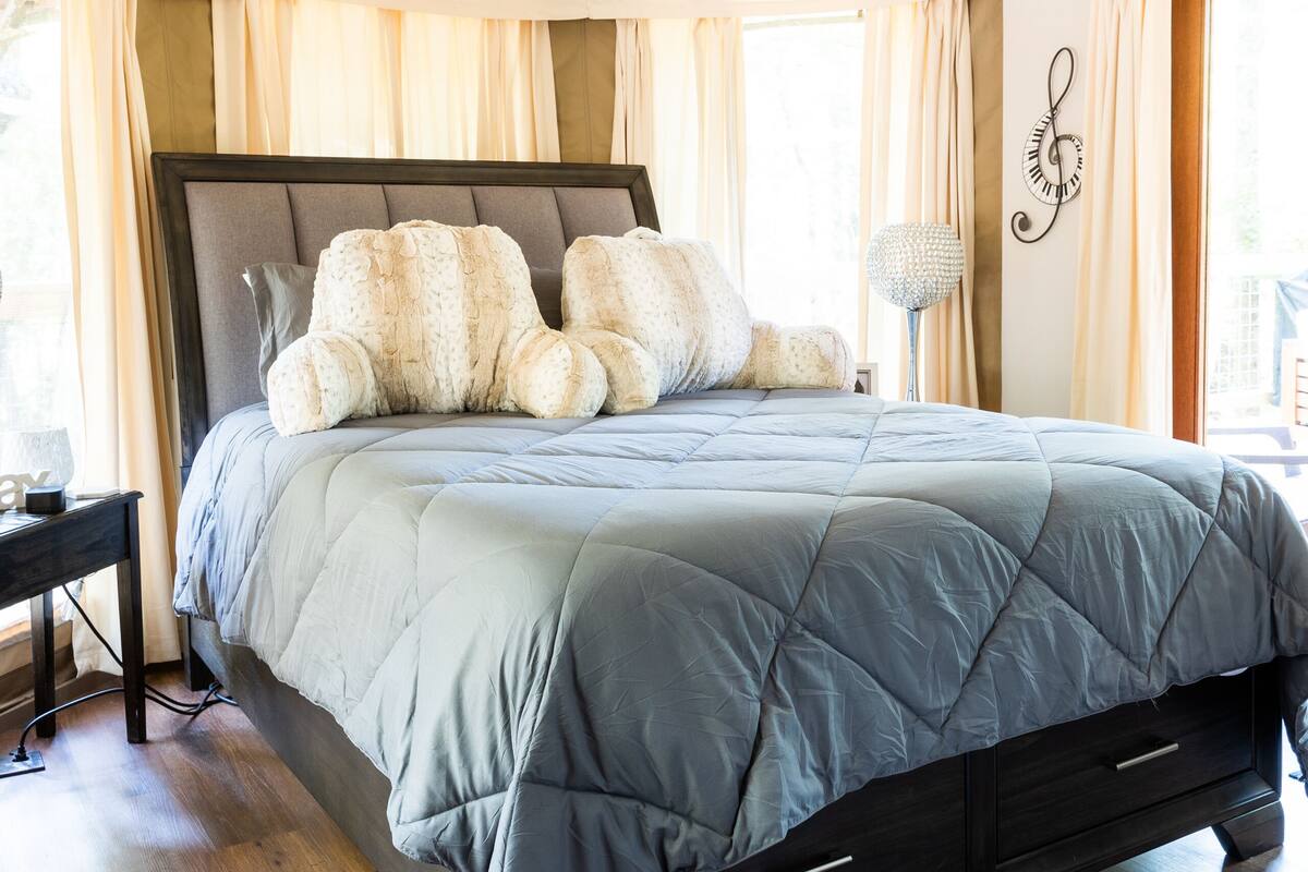 A bedroom with a bed, wooden flooring, a ceiling fan, and a window with curtains.