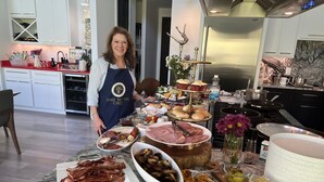 Una cocina con encimera de mármol llena de diversos alimentos y una mujer con delantal.