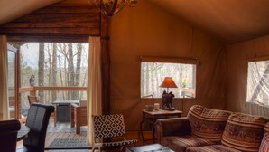 Interior acogedor de una cabaña con una terraza de madera, un sofá, una mesa de comedor y una lámpara.