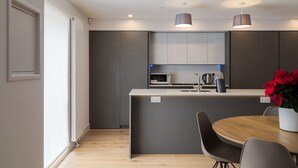 Une cuisine moderne avec des meubles gris, un four à micro-ondes et un évier. On y trouve une table à manger en bois, des chaises et un vase rempli de fleurs rouges.