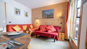 Ein gemütliches Zimmer mit Holzwand, einem roten Sofa und einem Esstisch mit Tellern und Besteck.
