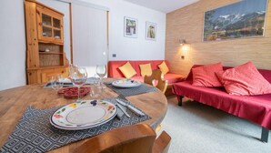 Ein gemütliches Wohnzimmer mit einem roten Sofa, einem Holzespeisetisch für zwei Personen und einem Holzschrank mit Glastüren.