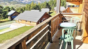 Un balcone in legno con vista su un paesaggio montuoso, un piccolo tavolo e una sedia.
