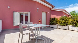 Eine Terrasse mit Tisch und Stühlen, einem Getränk in einem Glas und einem Gebäude mit einer rosafarbenen Fassade.