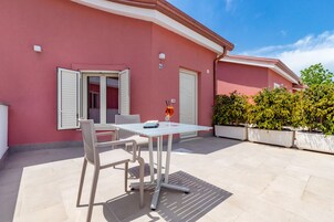 Un patio con una mesa, sillas, un vaso de bebida y un edificio de fachada rosa.
