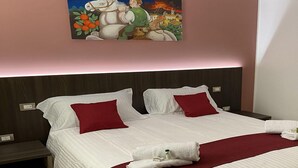 Ein Doppelbett mit weißer Bettwäsche und roten Kissen, ein Nachttisch und ein an der Wand hängendes Bild.