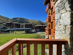 A hotel with stone and wooden architecture, a green lawn, and a view of a ski lift and mountains. - Ski-in/ski-out & foot of the slopes, 2nd floor, view ski slopes, balcony, tv, ski locker, 32m² (Valmorel)