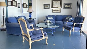 A room with a blue sofa set, matching armchairs, a round glass coffee table, and framed artwork on the walls. - Agi Avenida 5A Apartamento for rent in Roses Girona. (Roses)