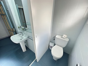Un baño con lavamanos blanco, inodoro y repisas de vidrio.