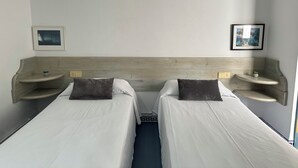 A hotel room with two single beds, wooden headboards, bedside tables with small plants, and framed pictures on the walls. - Agi Avenida 5A Apartamento for rent in Roses Girona. (Roses)