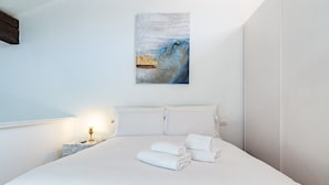 A neatly made bed with white linens and towels, a marble nightstand with a lamp, and a painting on the wall.