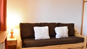 A wooden-framed sofa with two white cushions against a plain wall. - 20m from ski slopes, 2nd floor, tv, ski locker, 19m², Méribel (Méribel - Les Allues)