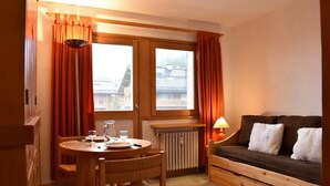 A cozy room with a wooden table set for two, a sofa with cushions, and a window with curtains. - 20m from ski slopes, 2nd floor, tv, ski locker, 19m², Méribel (Méribel - Les Allues)