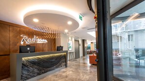 Un espace d’accueil d’hôtel avec un comptoir en marbre, un panneau lumineux et un design moderne au plafond.