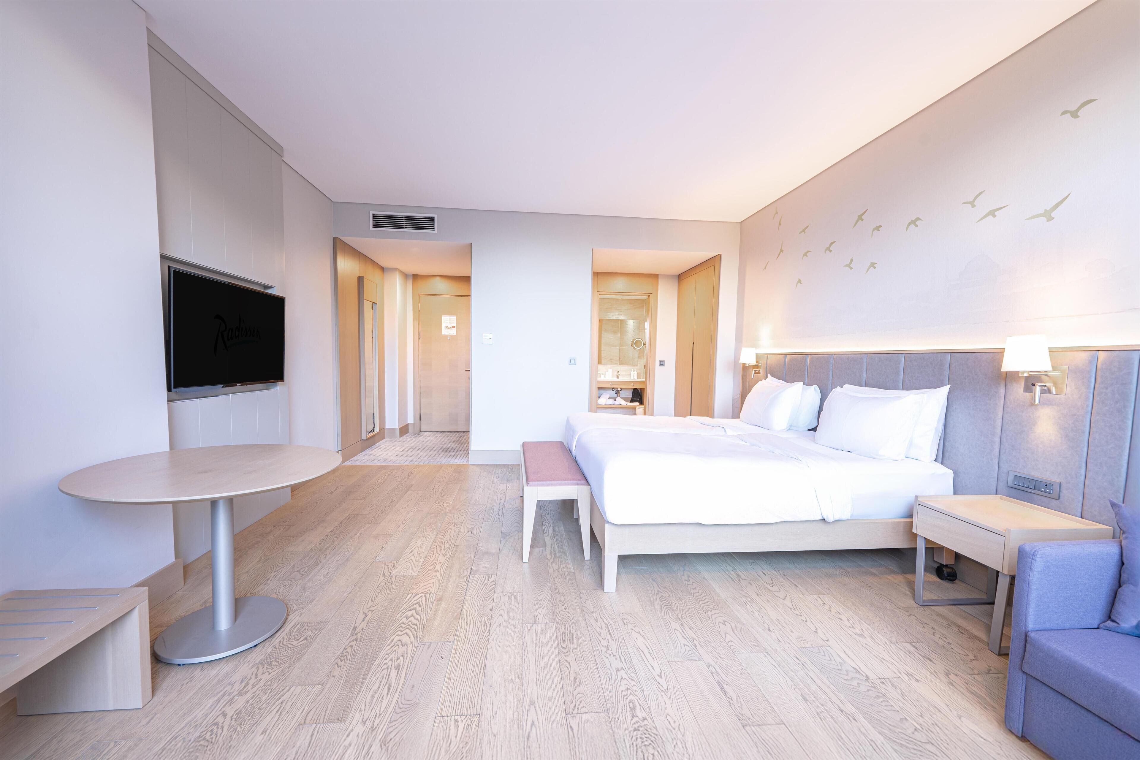 Ein Hotelzimmer mit Bett, Nachttisch, Stuhl, Fernseher und einem kleinen Tisch mit einer Bank.