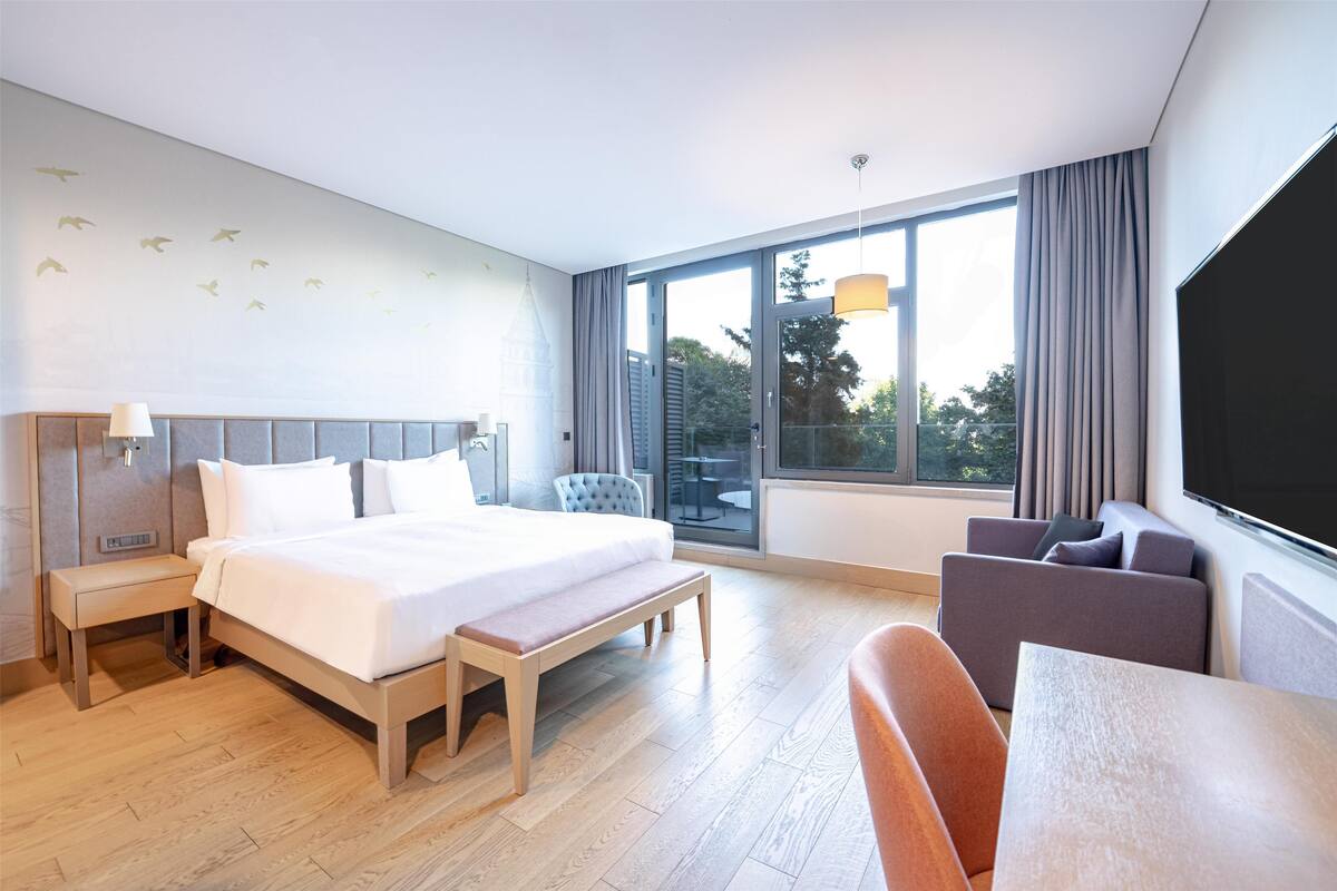 A modern hotel room with a large bed, a desk, and a sofa.