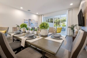 A dining area with a long table set for six, surrounded by chairs, with a large window offering a view of the outdoors. - Hidden Forest 3 Bedroom Vacation Home (2020) (Clermont)