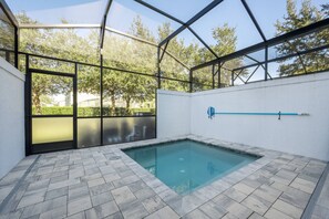 A swimming pool with a glass enclosure, surrounded by a herringbone-patterned floor, and a view of trees through the glass panels. - Hidden Forest 3 Bedroom Vacation Home (2020) (Clermont)