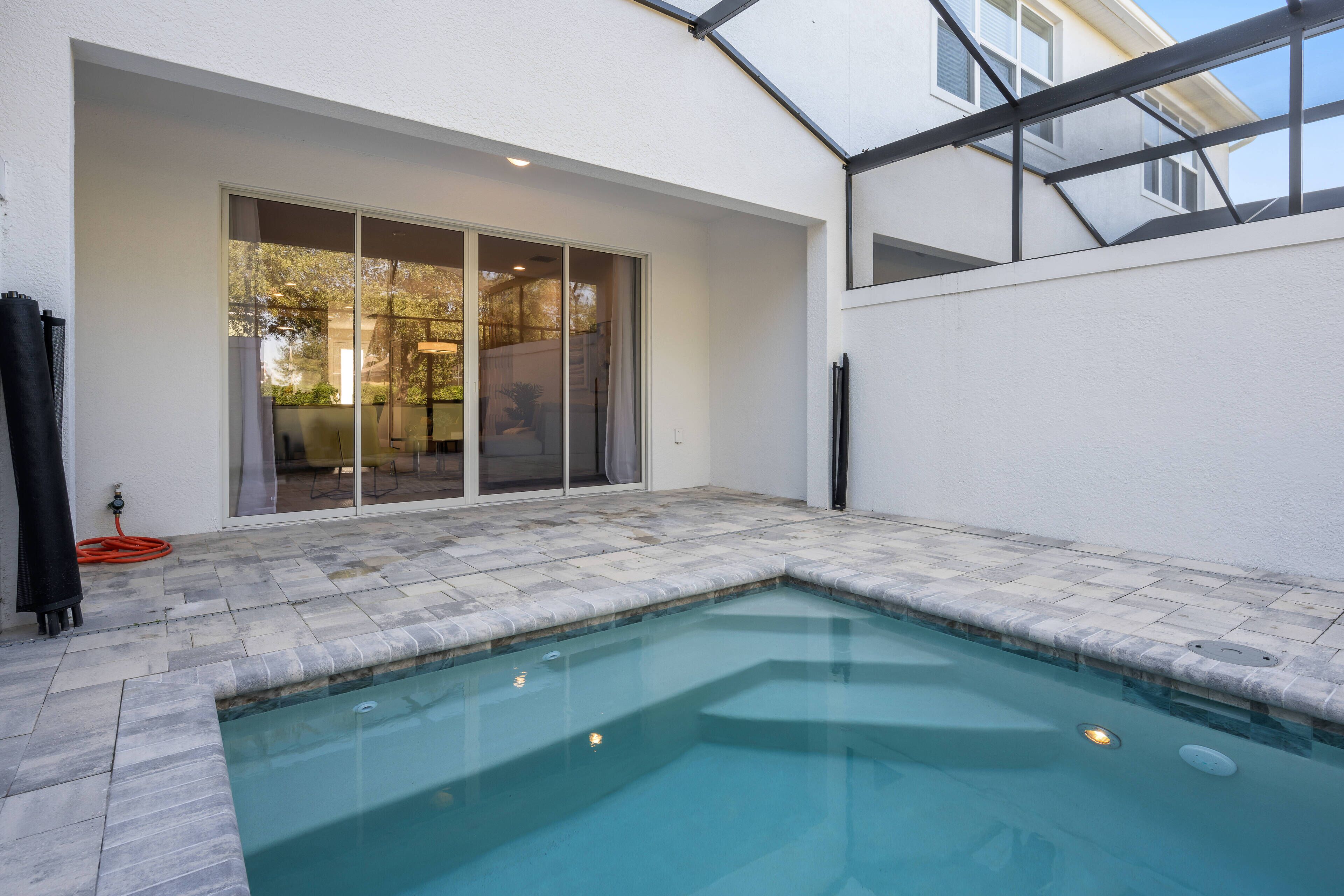 A swimming pool with a tiled deck, a sliding glass door, and a covered patio area.