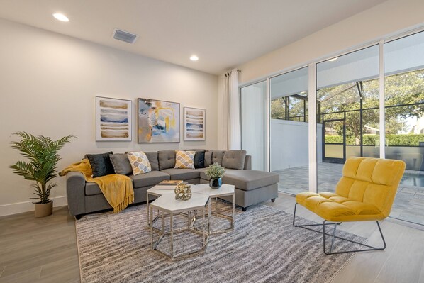 A modern living room with a grey sectional sofa, a yellow armchair, and a coffee table with a vase. - Hidden Forest 3 Bedroom Vacation Home (2020) (Clermont)