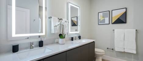 Een moderne badkamer met twee wasbakken, een grote spiegel, een toilet en een bad.