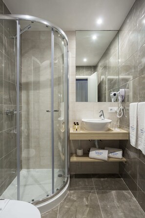 A modern bathroom with a glass-enclosed shower, a sink with a mirror above it, and a towel rack with towels. - Predicados do Douro Palace (Porto)