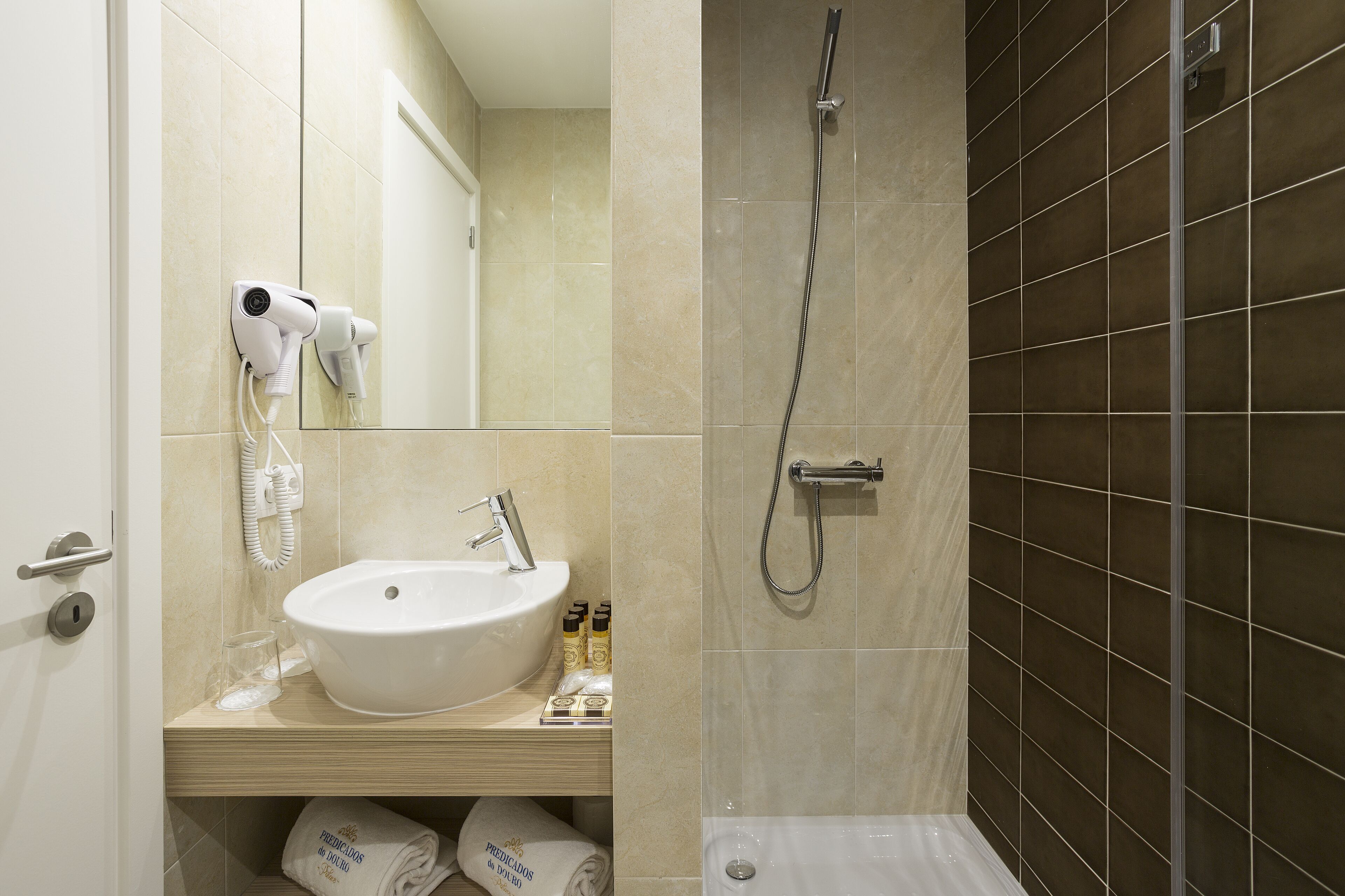 A bathroom with a sink, mirror, hairdryer, and shower.
