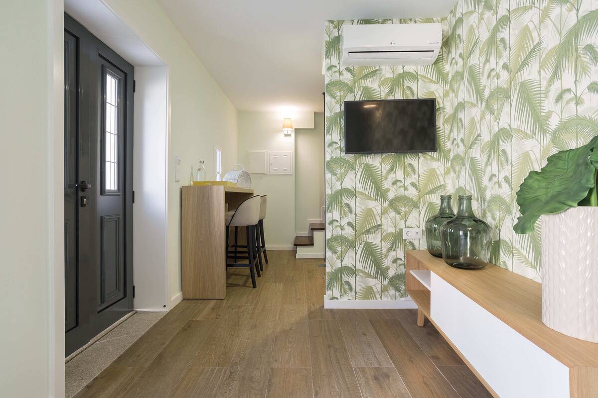 A hallway with a wooden bench, a TV mounted on the wall, and a large plant.