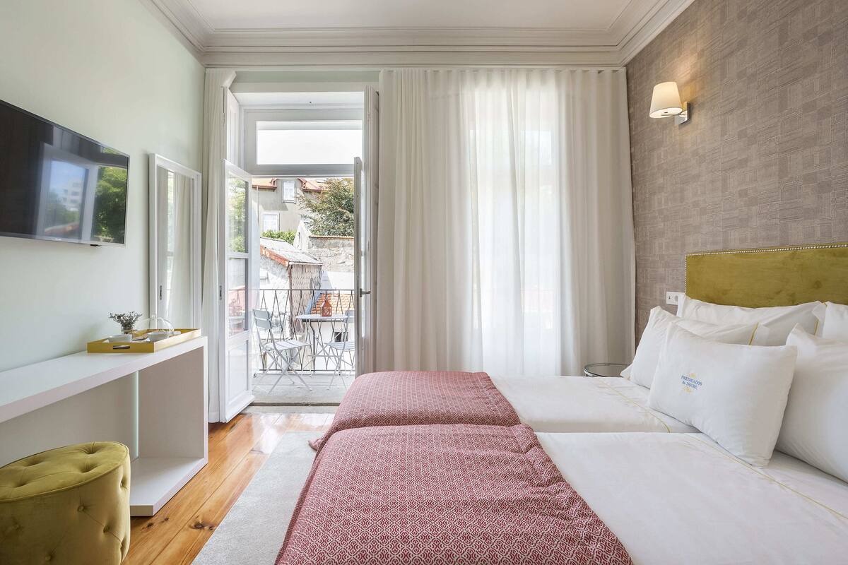 A hotel room with a bed, a TV, a desk, and a window with curtains.