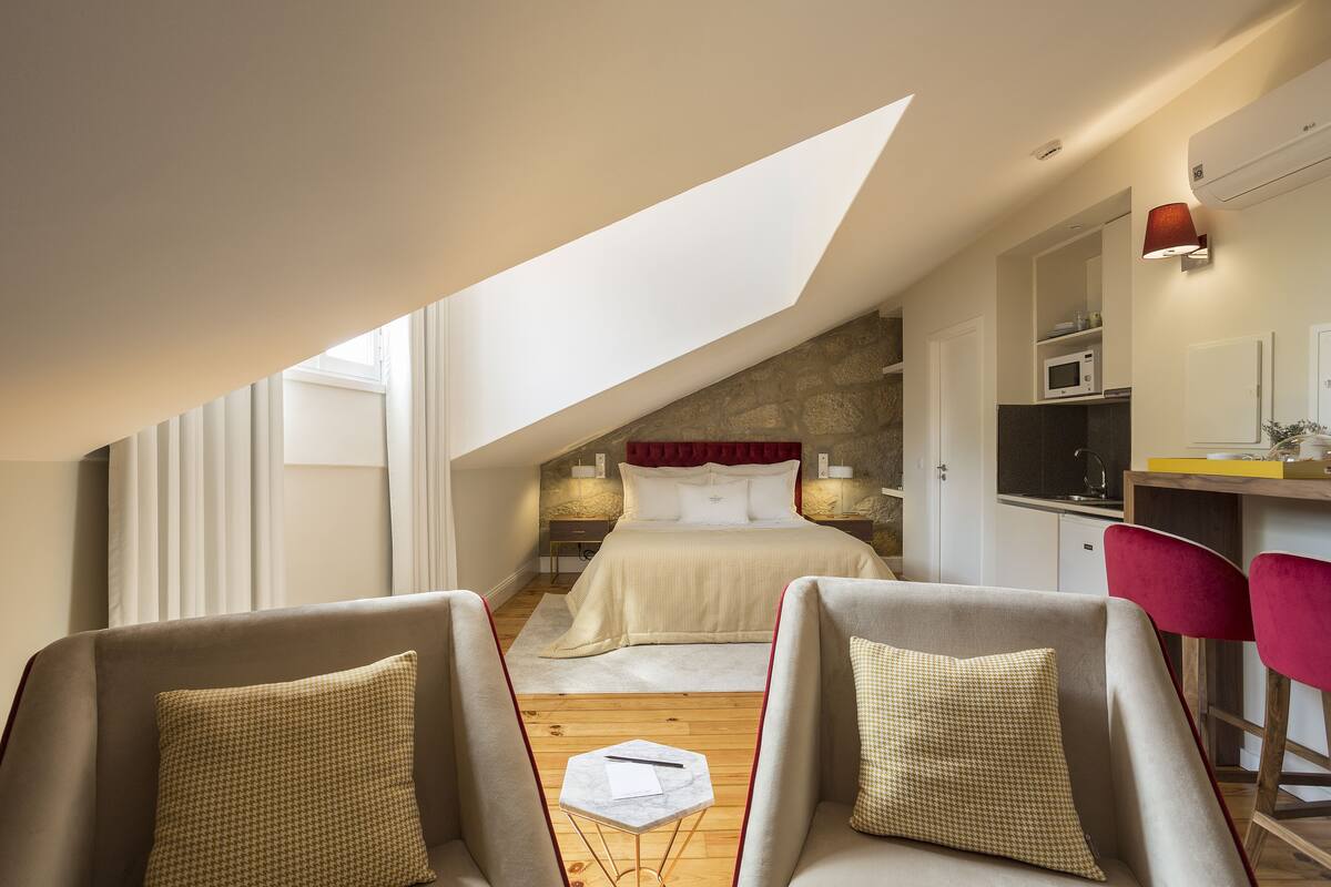 A bedroom with a sloped ceiling, a bed, a desk, and two chairs.