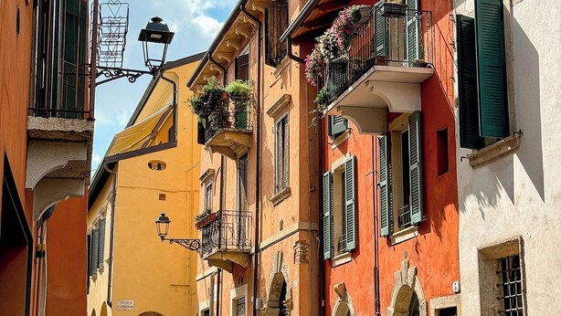 Una stretta strada acciottolata fiancheggiata da edifici colorati, con balconi adornati da fioriere e architettura tradizionale.