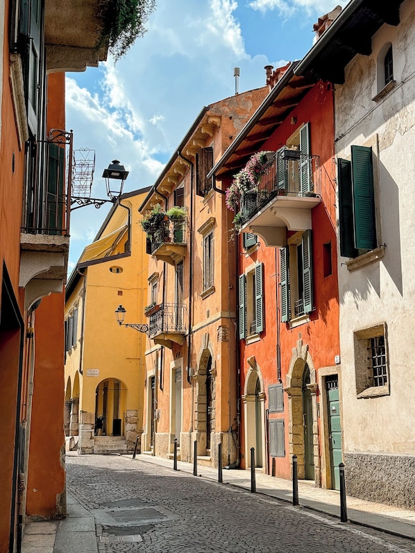 A narrow cobblestone street lined with colorful buildings, featuring balconies with flower boxes and traditional architecture.