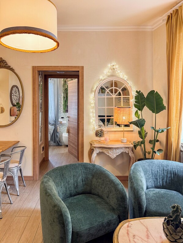 A cozy room with a wooden door leading to a bathroom, a vanity with a mirror, and a table with a lamp.