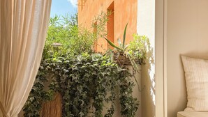 Una stanza con vista su un edificio, una panca verde, uno sgabello in vimini e una pianta pensile.