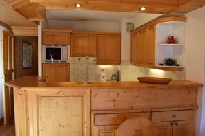 A kitchen with wooden cabinets, a built-in microwave, a coffee maker, and a decorative candelabra. - 2nd floor, view mountain, balcony, tv, ski locker, 51m², Méribel (Méribel - Les Allues)