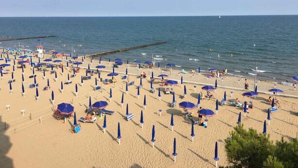 Une plage dotée de nombreux parasols et de chaises longues, d’une tour de surveillance pour les sauveteurs et d’une jetée qui s’avance dans l’eau.