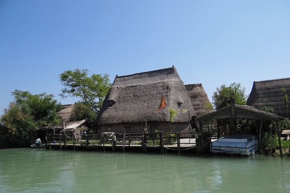 Thatched-roof huts with a wooden dock extending into a calm body of water.