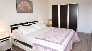 A bedroom with a bed, a nightstand, a lamp, a chair, and a wardrobe.