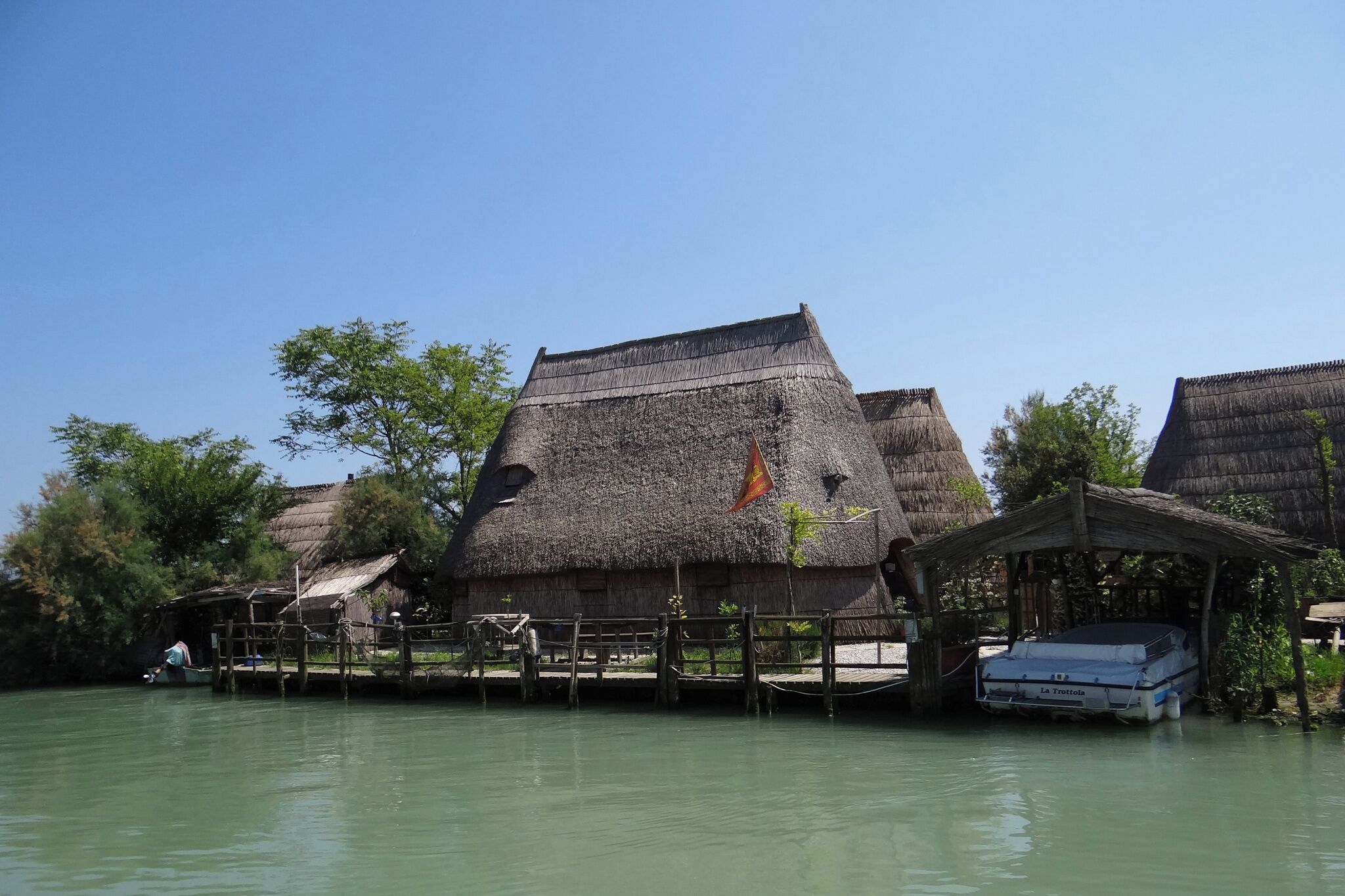 Thatched-roof huts with a wooden dock extending into a calm body of water.
